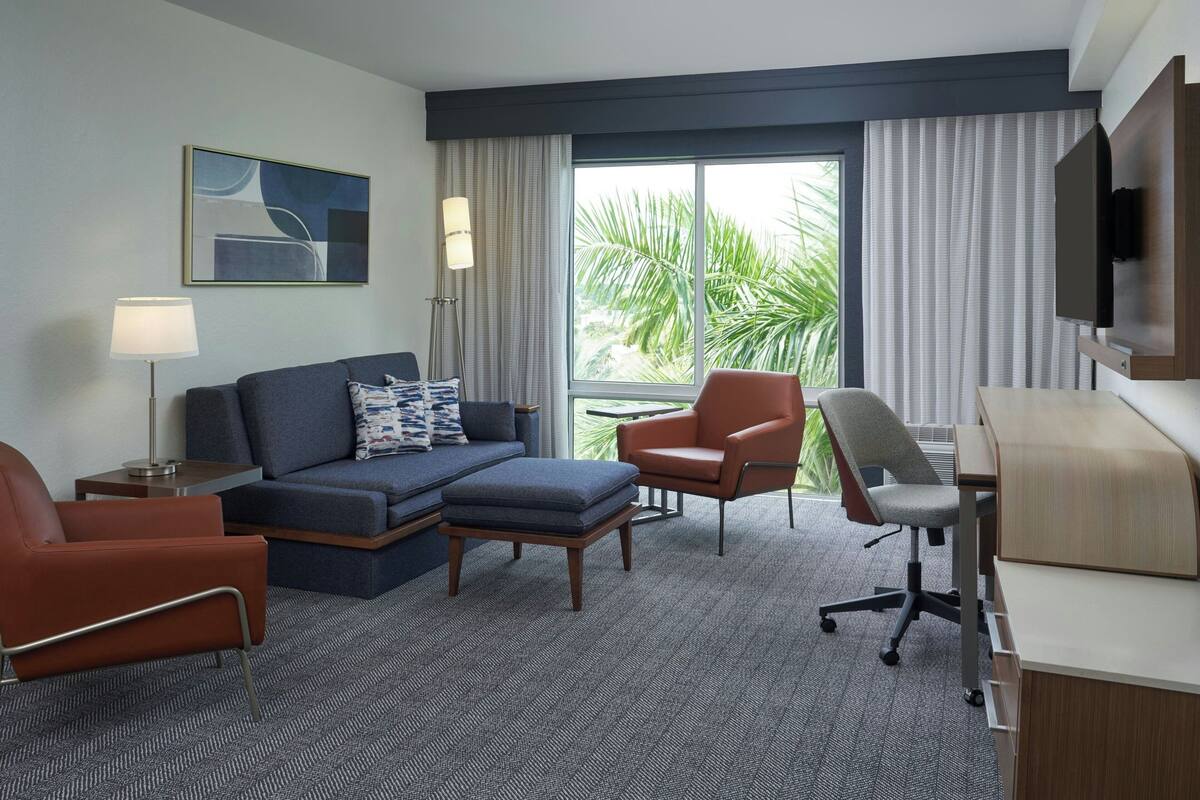 Une chambre d’hôtel avec un canapé, deux fauteuils, un bureau et une télévision.
