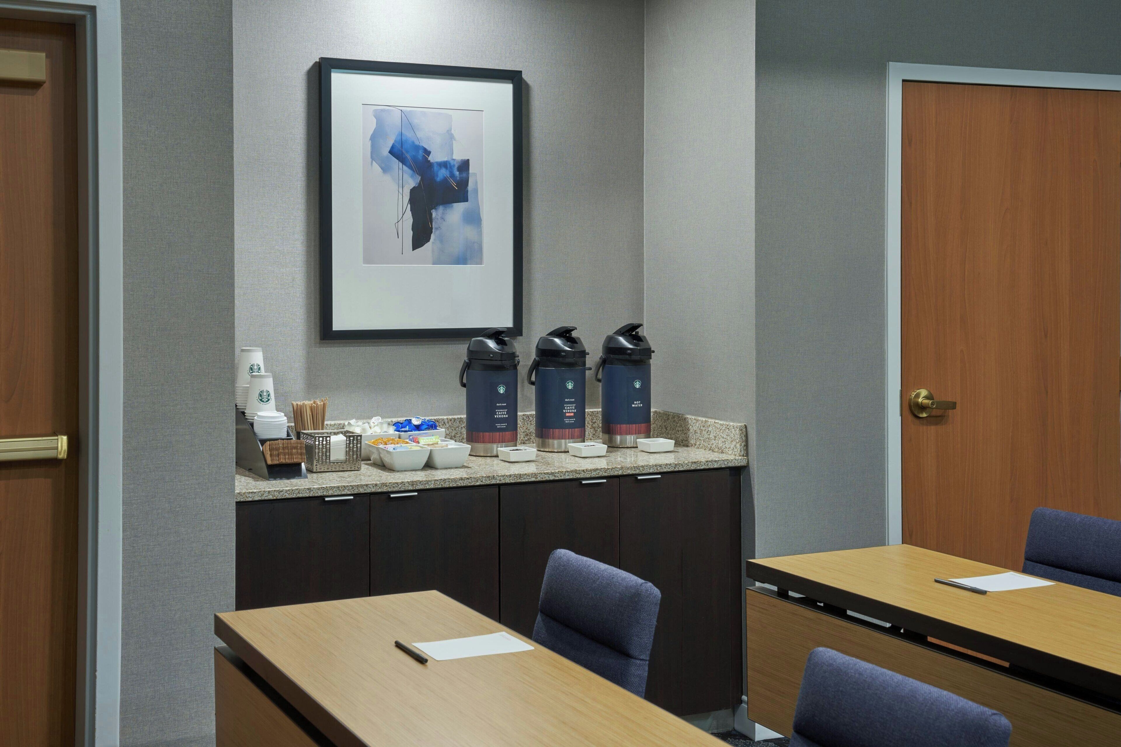 A conference room with a long table, chairs, a coffee station, and a framed artwork on the wall.