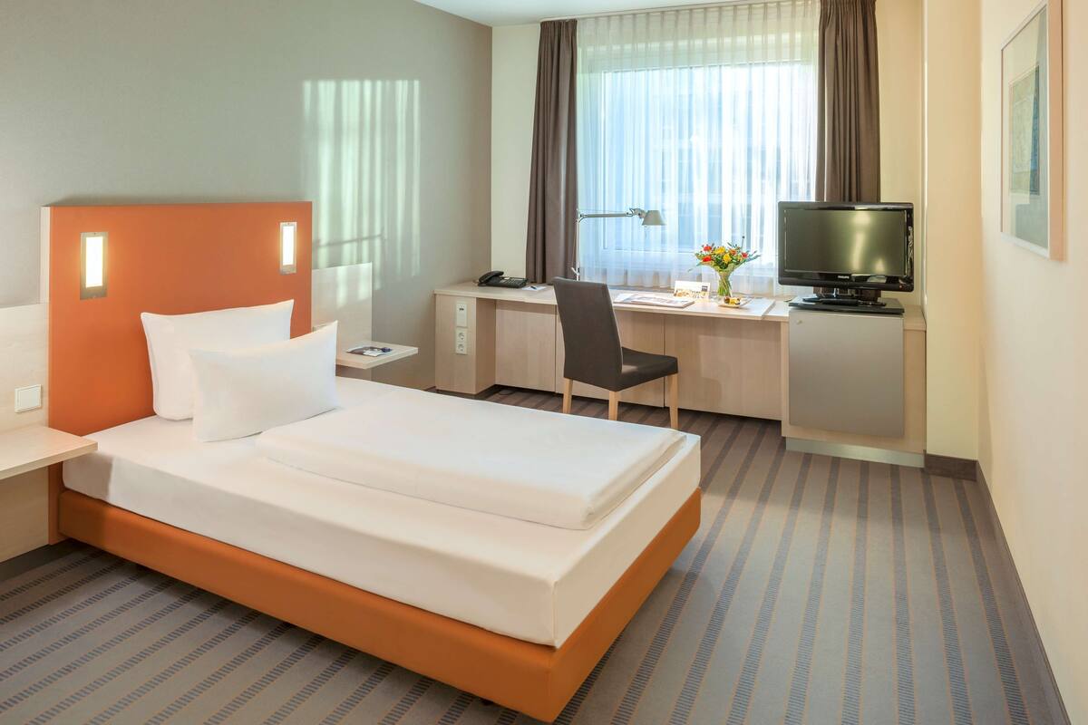 A hotel room with a bed, desk, chair, television, and a window with curtains.