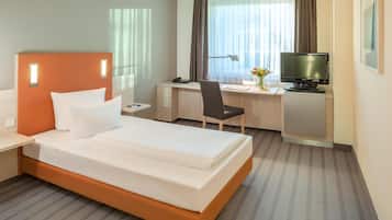 Habitación de hotel con cama, escritorio, silla, televisor y ventana con cortinas.