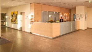 Un espace d’accueil d’hôtel au design moderne, comprenant un comptoir d’accueil, une grande peinture abstraite et un intérieur bien éclairé.