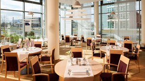 Un vaste espace dédié à la salle à manger, avec des tables et des chaises rondes, de grandes fenêtres et un éclairage moderne suspendu au plafond.