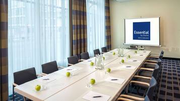 A conference room with a long table, chairs, a projector screen, and a view of the city through large windows.