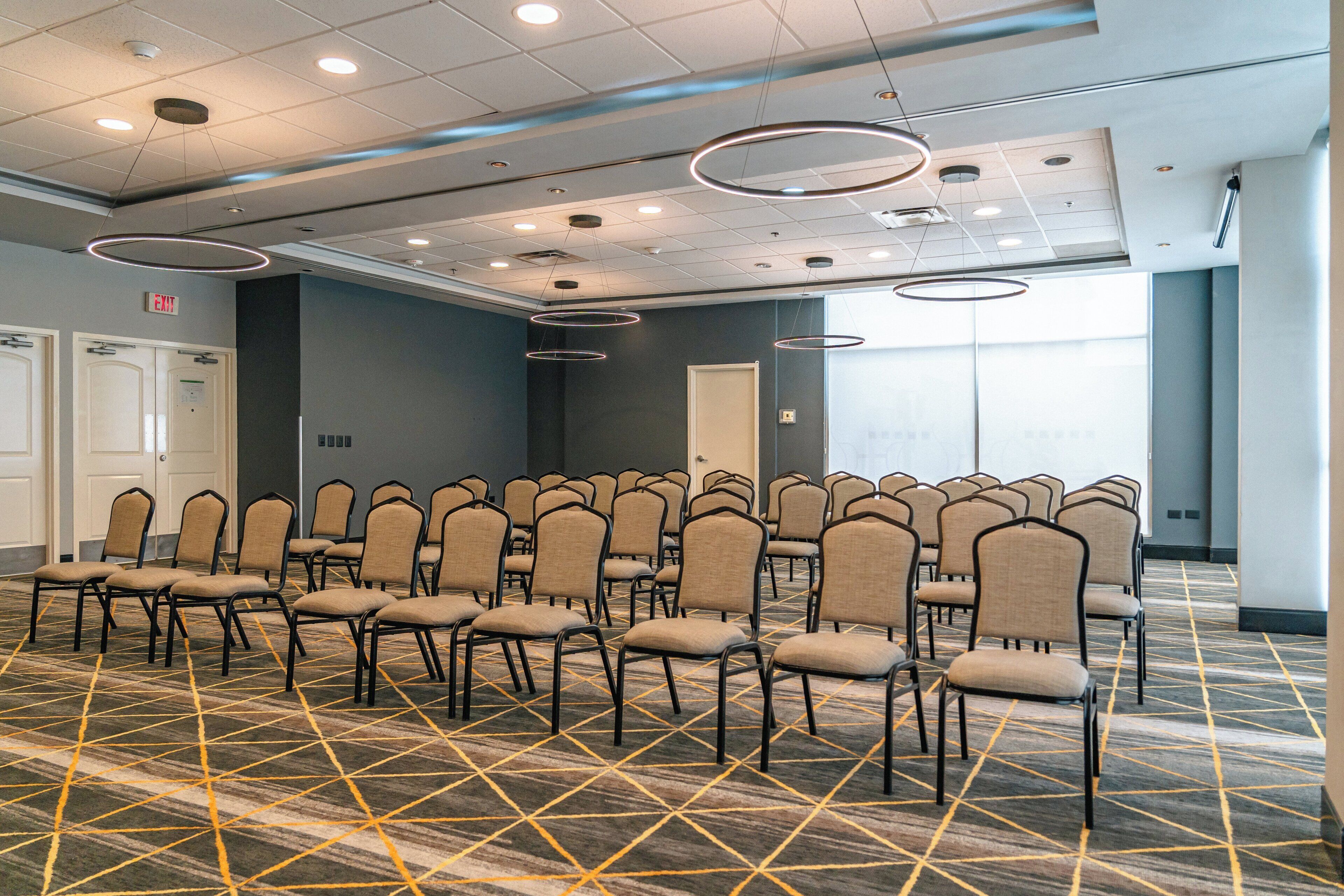 A conference room with rows of chairs, a patterned carpet, and ceiling lights.
