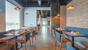 A modern restaurant with wooden tables and blue cushioned seating, brick walls, and pendant lighting.