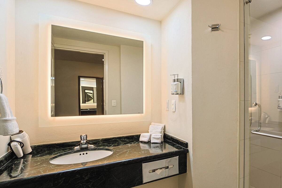 Un baño moderno con lavamanos de mármol, un espejo grande, una ducha con mampara de vidrio y un perchero para toallas.
