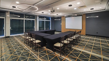 Un salón de conferencias con una gran mesa, sillas, un proyector y una pantalla.