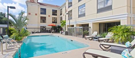 A swimming pool with lounge chairs and umbrellas, surrounded by a building with multiple floors and balconies.