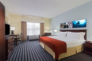 Habitación de hotel con una cama grande, un escritorio con silla, televisión y ventana con cortinas.