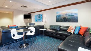 A modern hotel room with a black leather sofa, a small round table, and a flat-screen TV mounted on the wall.