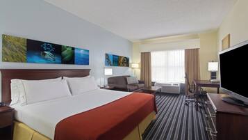 Habitación de hotel con una cama grande, un escritorio con televisor de pantalla plana, un sofá y una ventana con cortinas.