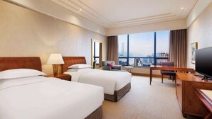 A hotel room with two beds, a desk, a TV, and a large window with a city view. - Hilton Chongqing Hotel (Chongqing)
