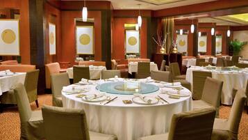 Une salle à manger élégante, avec des tables rondes dressées pour accueillir plusieurs convives, agrémentée de nappes blanches et de touches dorées.