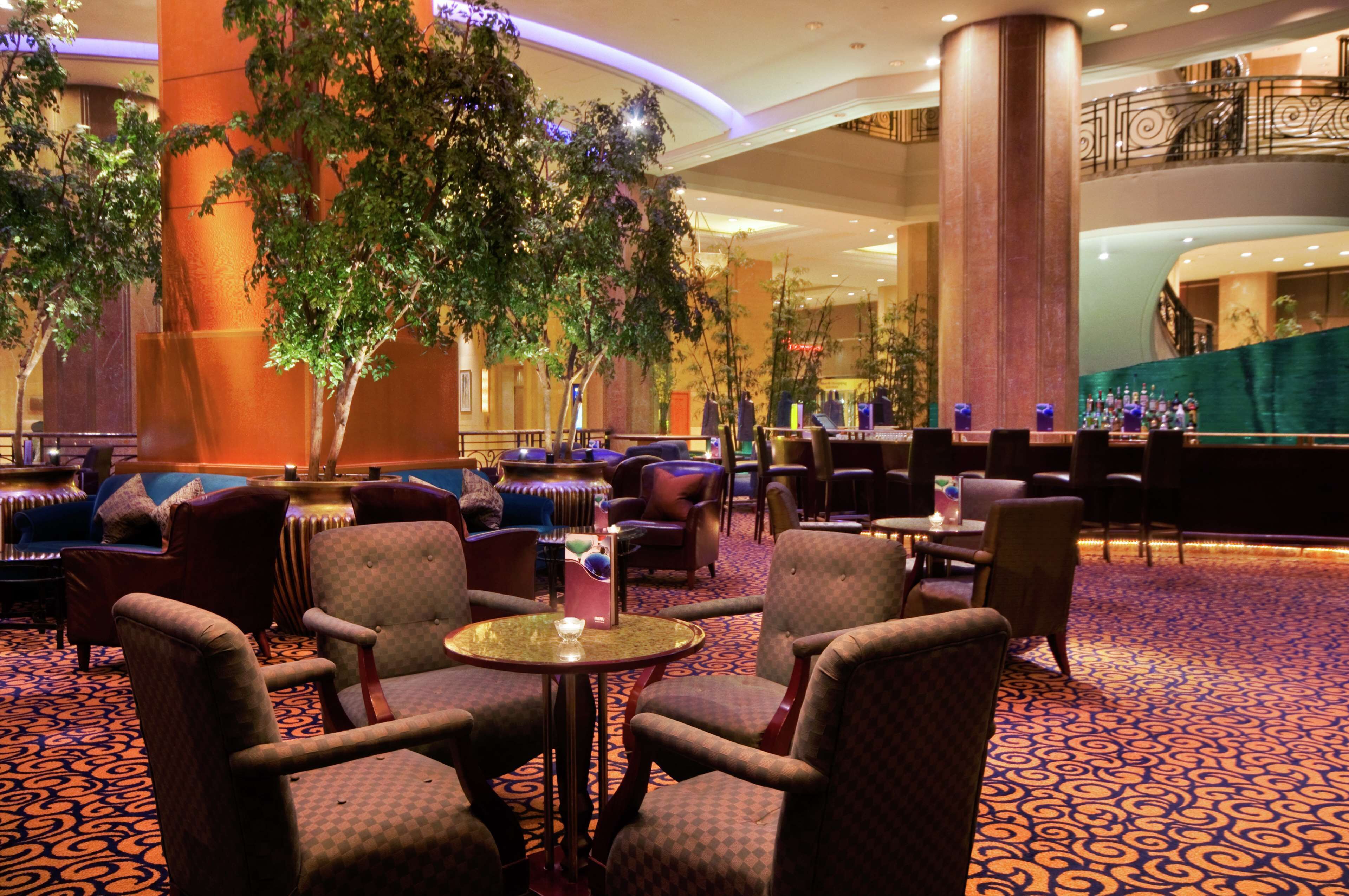 A hotel lobby with a large indoor tree, comfortable seating, and a bar area.