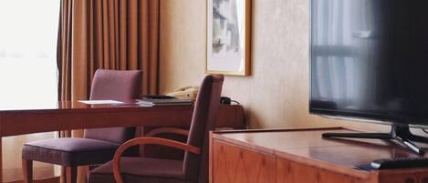 A hotel room with a wooden desk, two chairs, a television, and a framed picture on the wall.