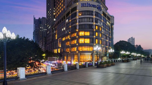 A tall hotel building with illuminated windows and a prominent Hilton logo. - Hilton Chongqing Hotel (Chongqing)