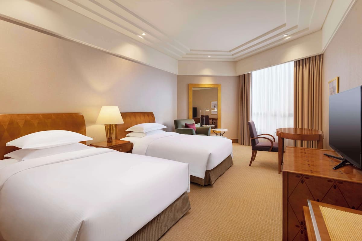 Een hotelkamer met twee bedden, een televisie, een bureau en een spiegel.