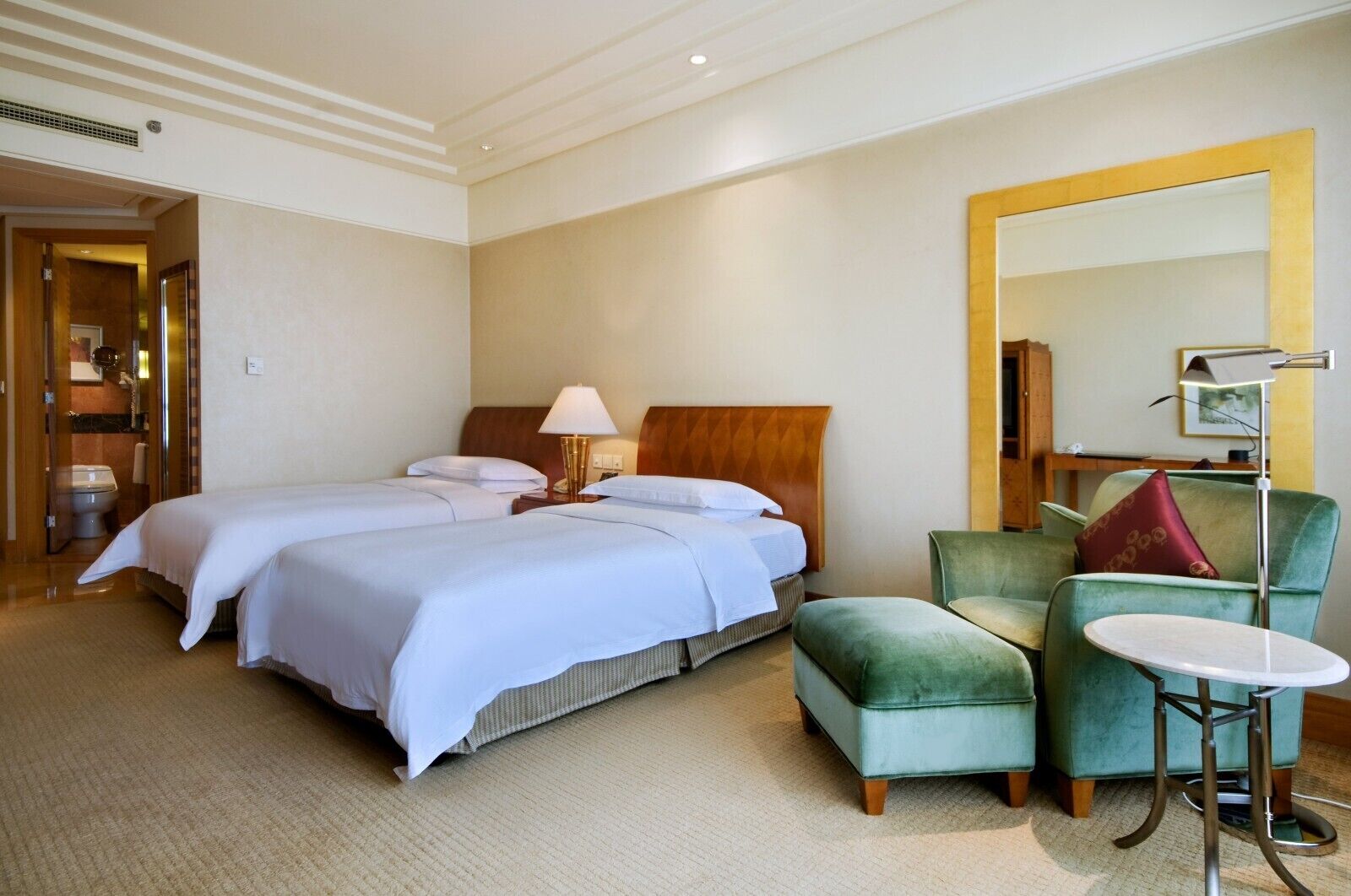 Een hotelkamer met twee bedden, een groene fauteuil, een klein rond tafeltje en een grote spiegel.