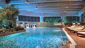An indoor swimming pool with a checkered tile pattern, surrounded by lounge chairs and potted plants. - Hilton Chongqing Hotel (Chongqing)