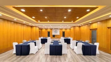 A conference room with multiple tables, white chairs, and a projector screen displaying the Hilton logo.
