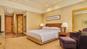 Habitación de hotel con una cama grande, una mesita de noche con lámpara, una silla y una obra de arte colgada en la pared.