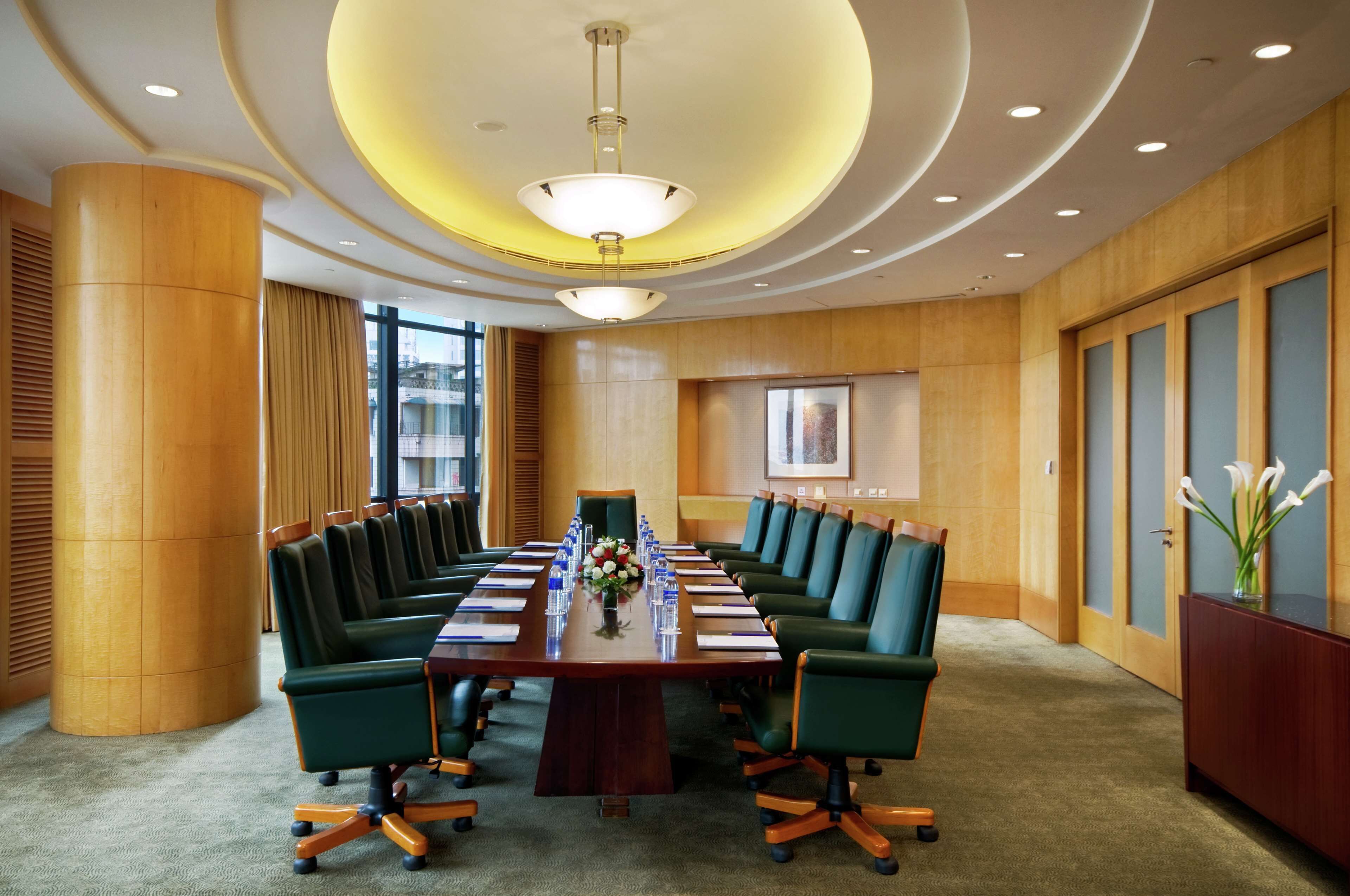 A conference room with a long table, green chairs, and a chandelier.
