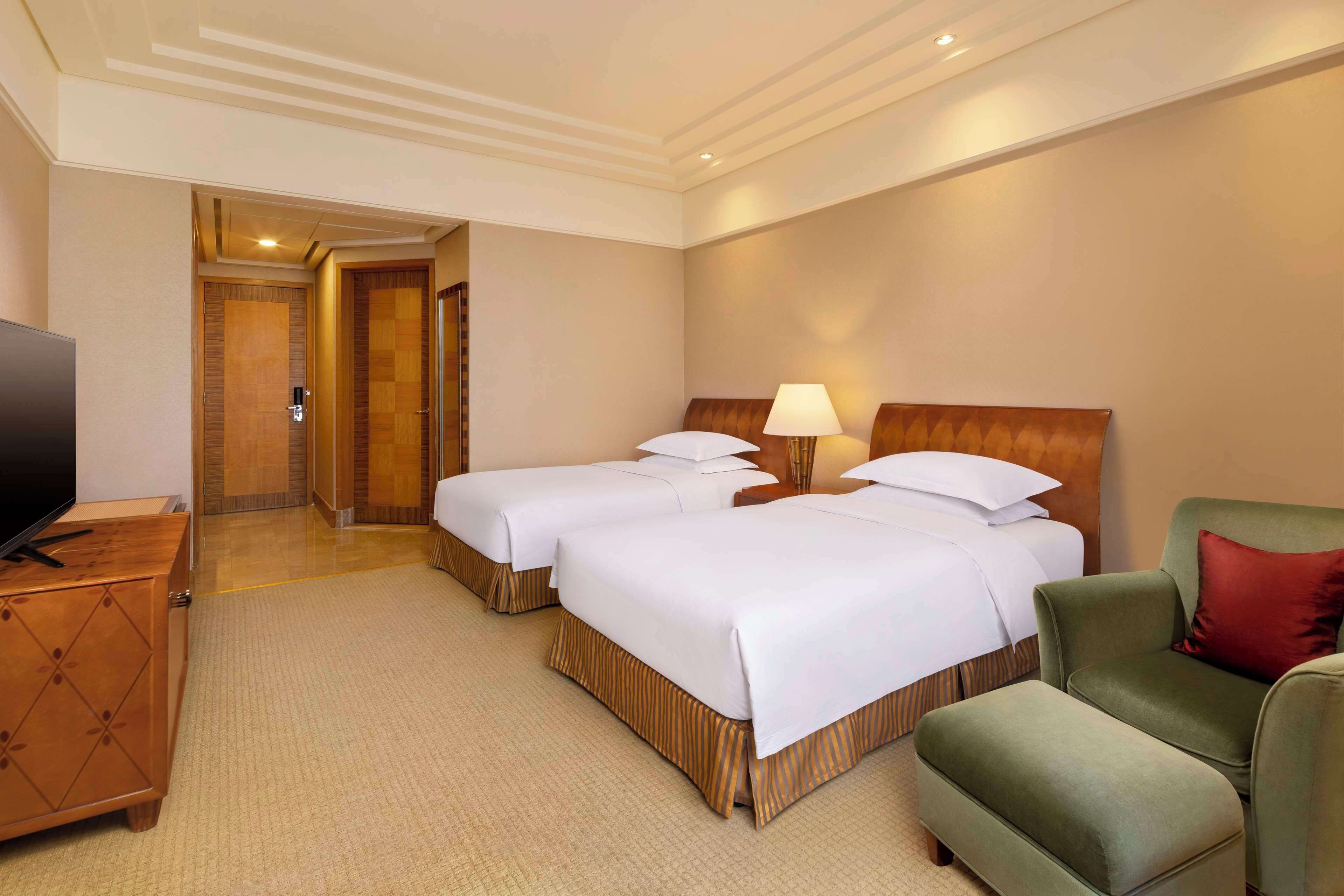 Een hotelkamer met twee bedden, een televisie, een bureau en een groene fauteuil.