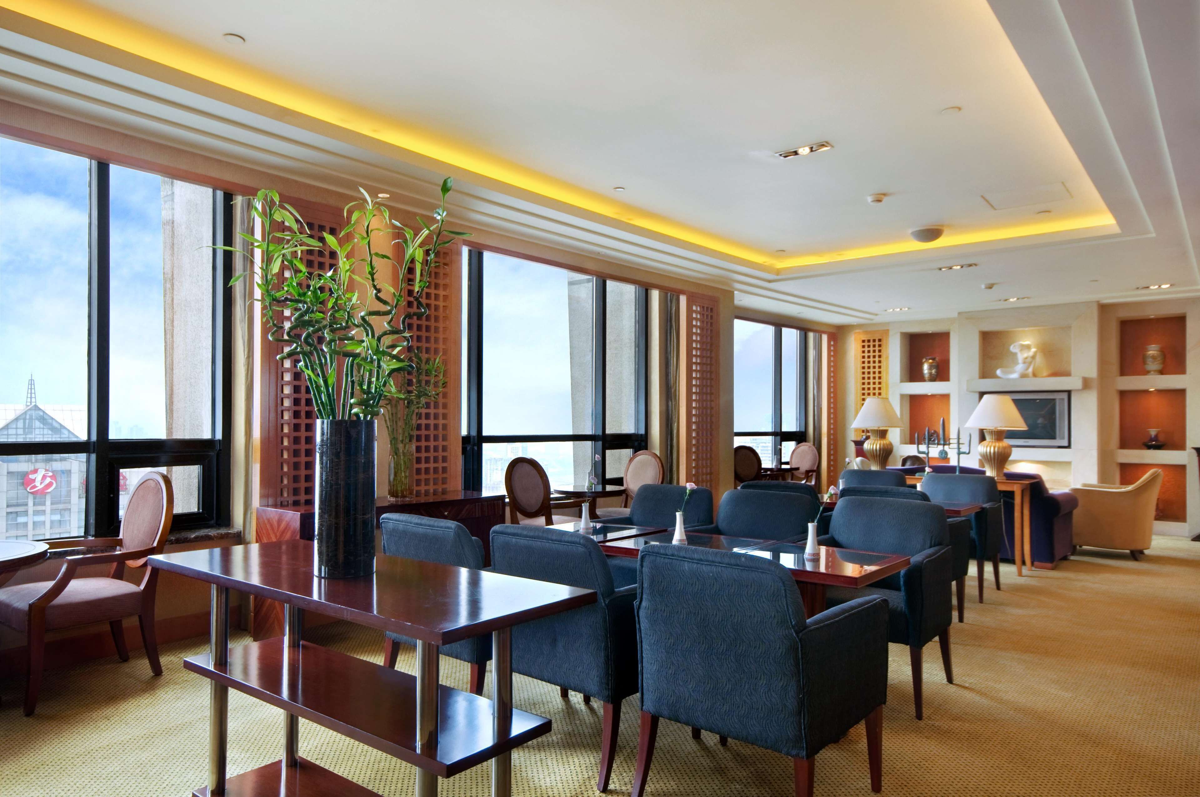 Un salón de conferencias de hotel con ventanas amplias, una planta en maceta y mobiliario moderno.