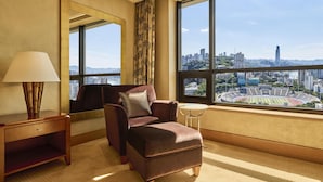 A hotel room with a large window offering a city view, a comfortable armchair, a small round table, and a lamp. - Hilton Chongqing Hotel (Chongqing)