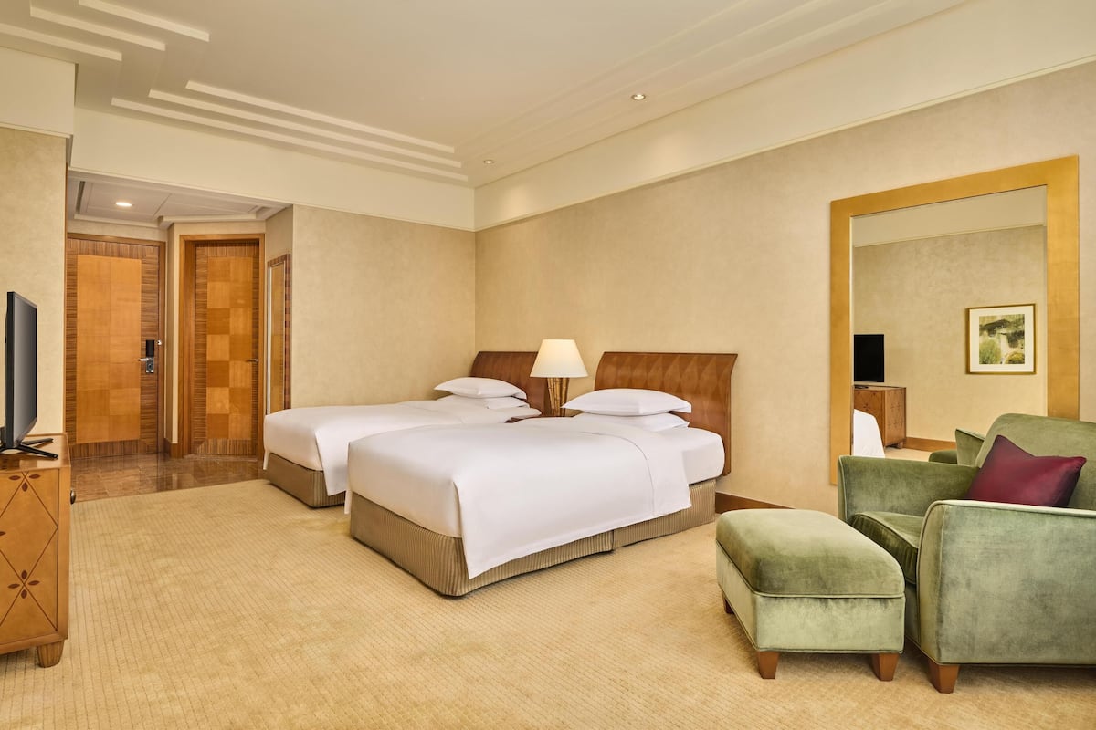 Een hotelkamer met twee bedden, een groene fauteuil, een televisie en een grote spiegel.