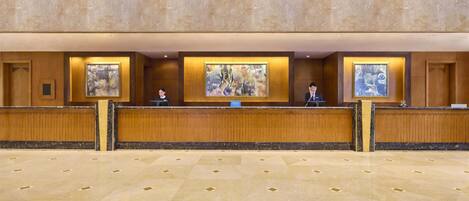 A reception area with a marble floor, wooden reception desk, and three framed artworks above the counter.