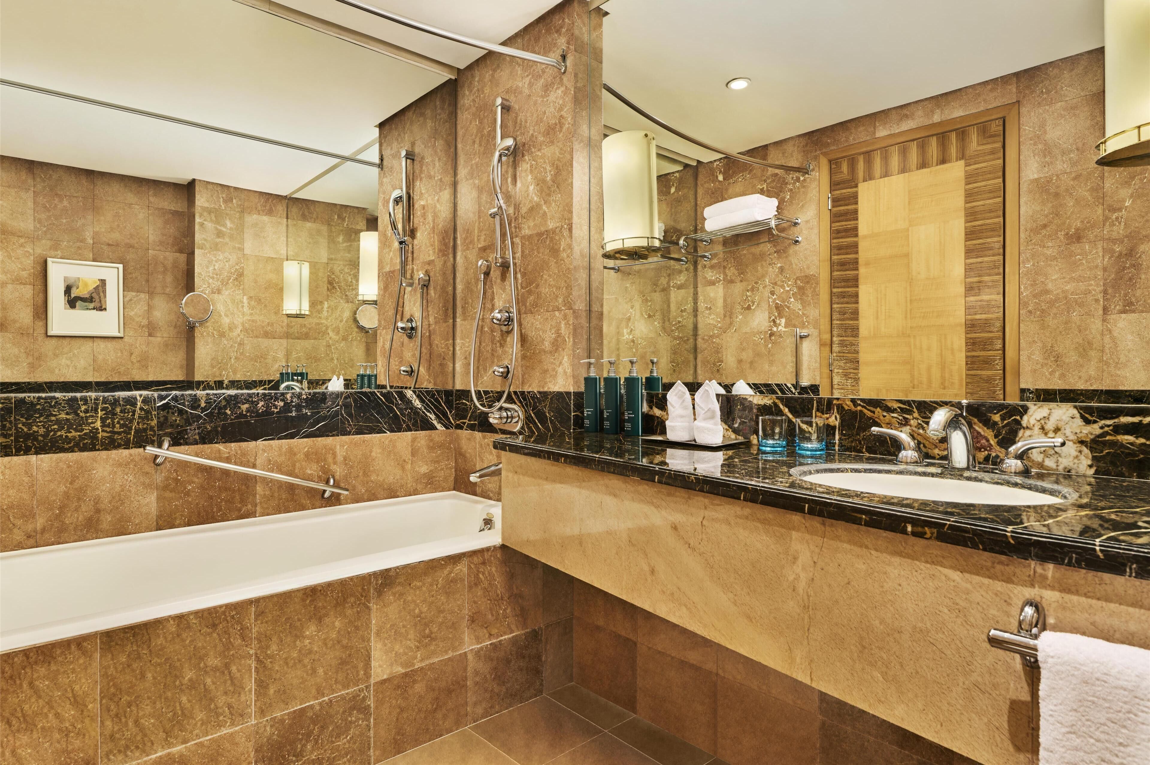 A modern bathroom with a large mirror, a bathtub, a sink, and a shower.