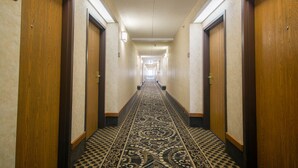 Un pasillo de hotel con puertas de madera, alfombra estampada y un letrero con número en la pared.