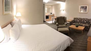 A hotel room with a large bed, a desk, a chair, a sofa, and a small table with a plant.