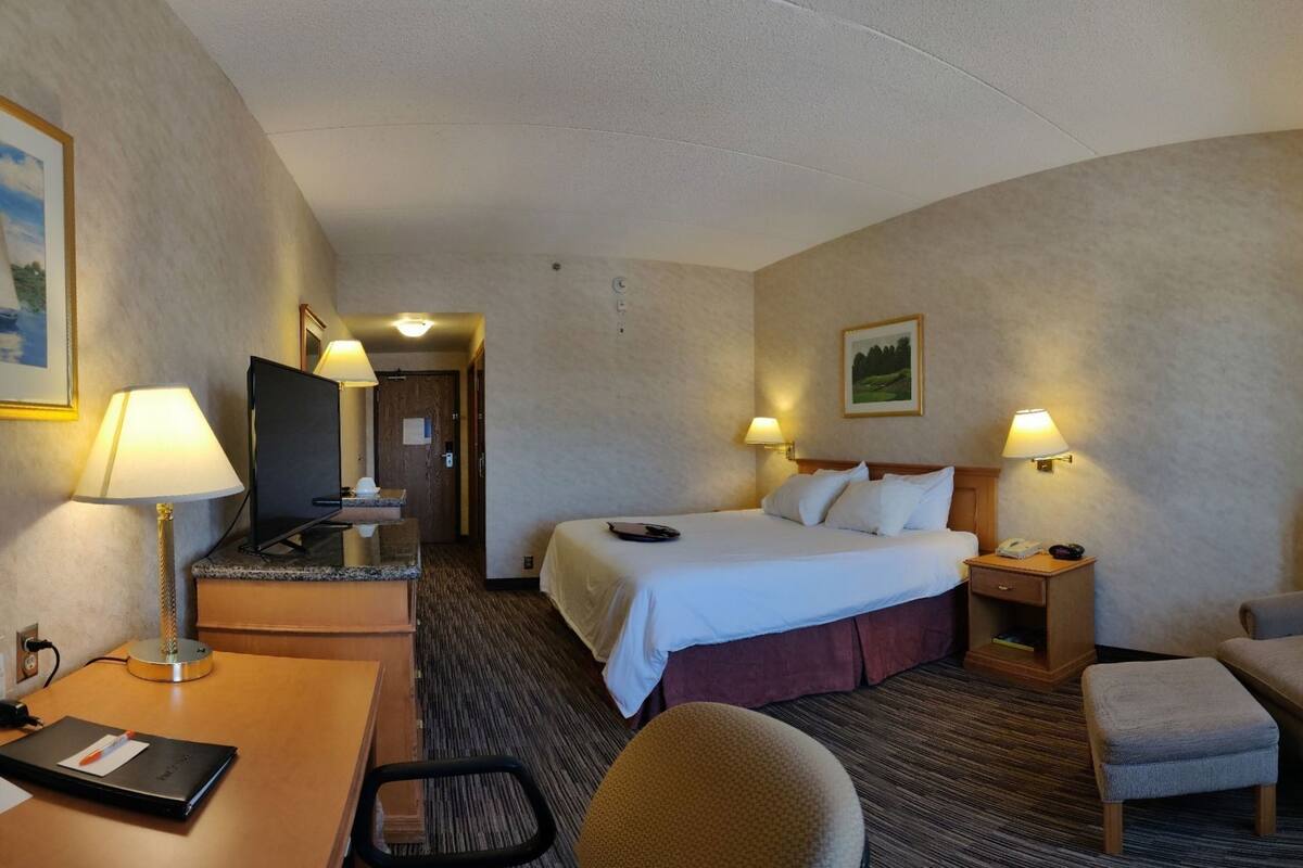A hotel room with a bed, desk, chair, and a television.