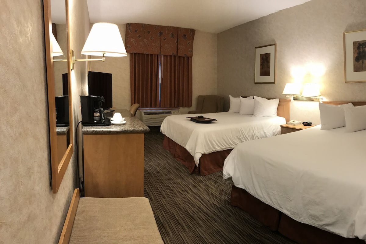 A hotel room with two beds, a desk with a coffee maker, a chair, and a large mirror.