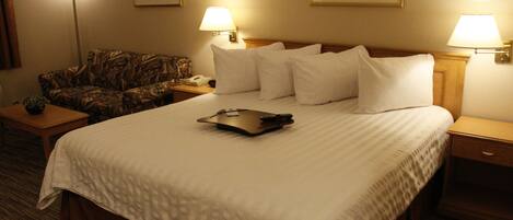 A hotel room with a large bed, two bedside tables, a lamp, a telephone, and a floral-patterned sofa.