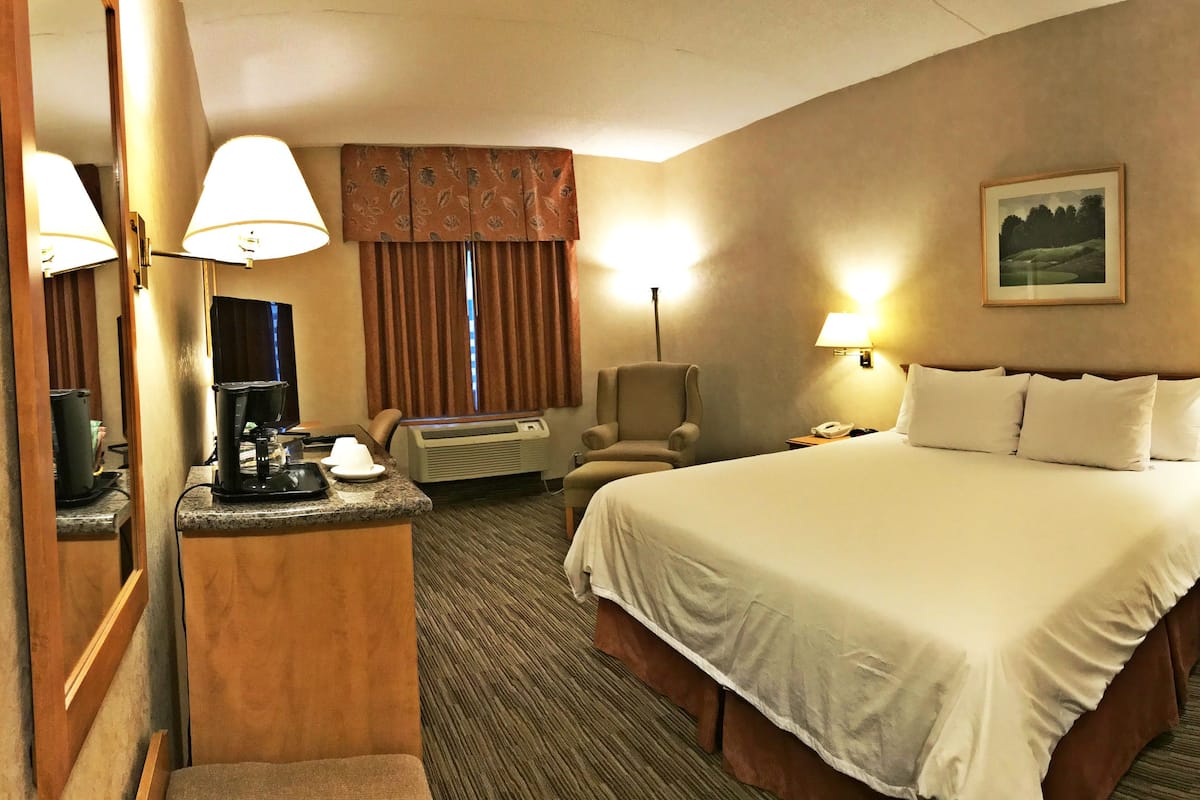 A hotel room with a large bed, two bedside lamps, a desk with a telephone, an air conditioning unit, and a chair.