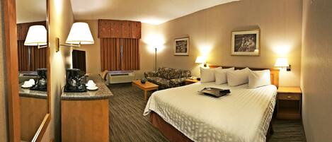A hotel room with a bed, bedside tables, a desk with a coffee maker, a lamp, and a painting on the wall.