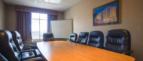 A conference room with a long table and six leather chairs, a whiteboard, and a painting on the wall.