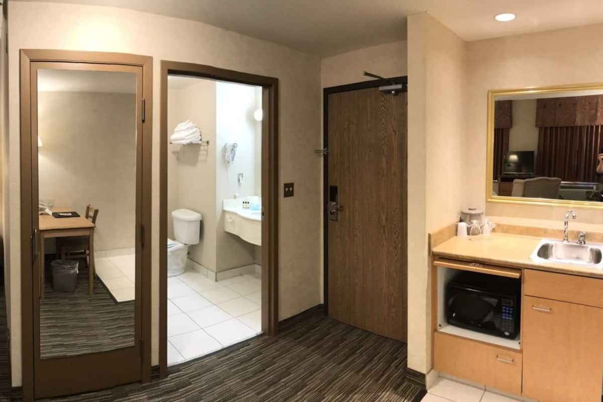 A hotel room with a bed, a desk, a TV, a sofa, a mirror, and a bathroom visible through an open door.