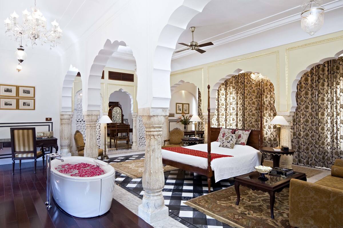Um quarto de hotel luxuoso com uma cama grande, um espaço de estar, uma banheira com pétalas de rosa e decoração requintada.
