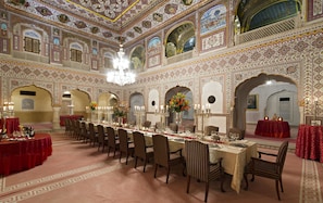 A grand dining hall with ornate ceiling and walls, multiple dining tables, and chandeliers.