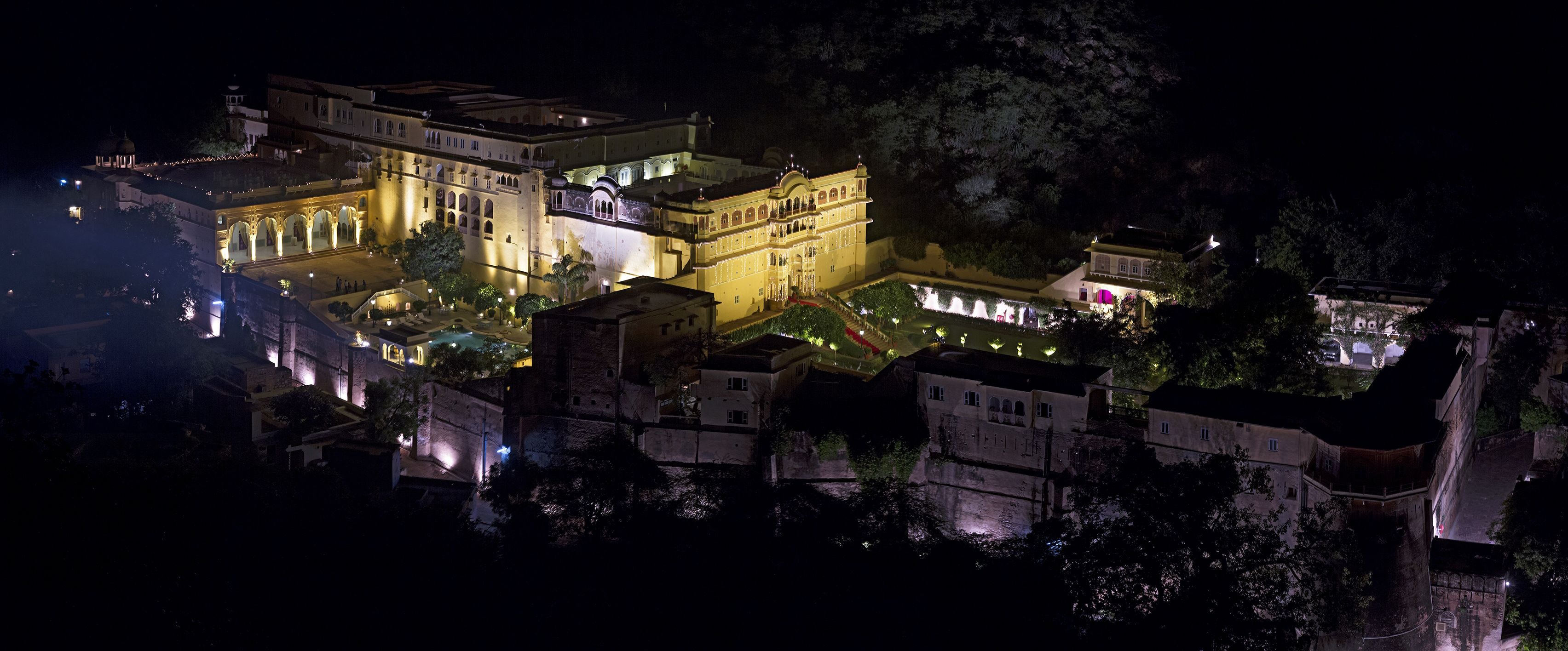 A large, illuminated building complex with multiple structures, including a prominent central building with arches and a smaller adjacent building.