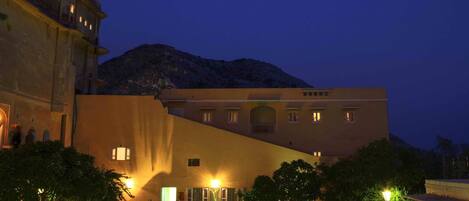 A nighttime view of a hotel with a swimming pool, outdoor seating, and a mountain in the background.