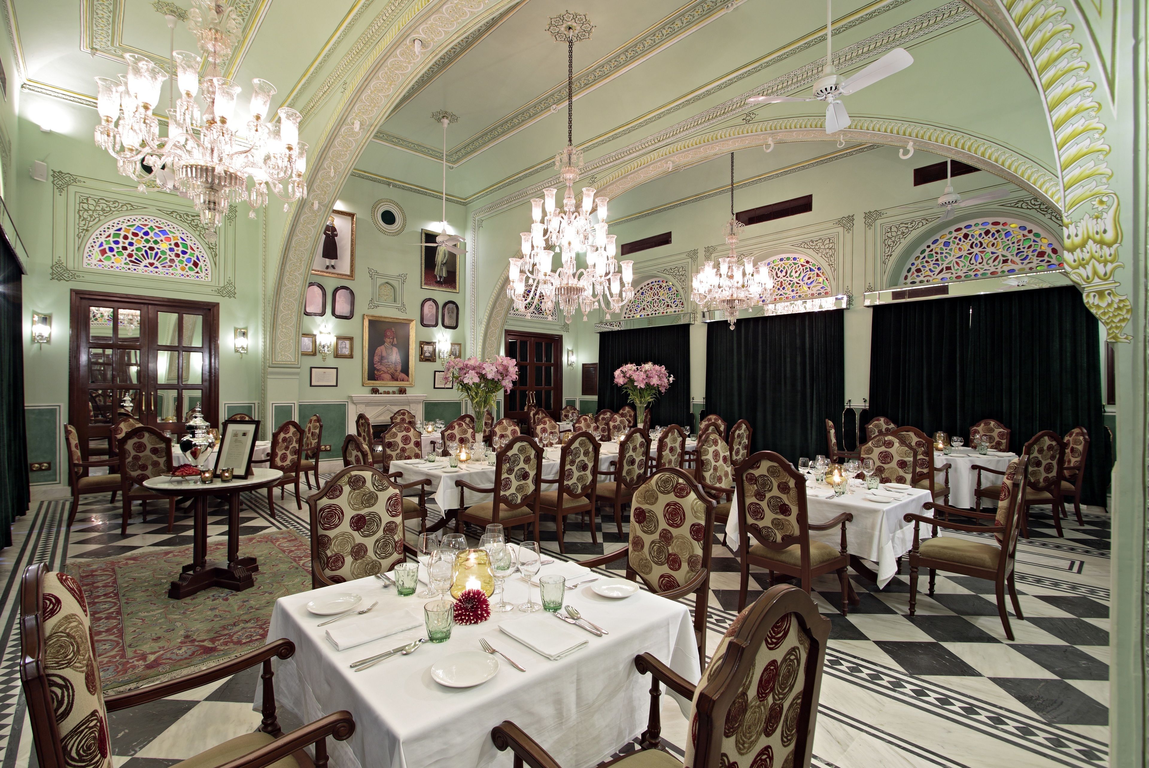 Una sala da pranzo formale con diversi tavoli e sedie, lampadari e decorazioni elaborate alle pareti.