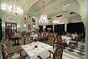 Una sala da pranzo formale con diversi tavoli e sedie, lampadari e decorazioni elaborate alle pareti.