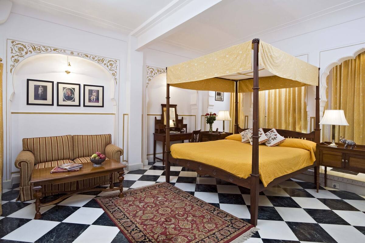 A four-poster bed with a canopy, a sofa, a wooden nightstand, and a patterned rug.