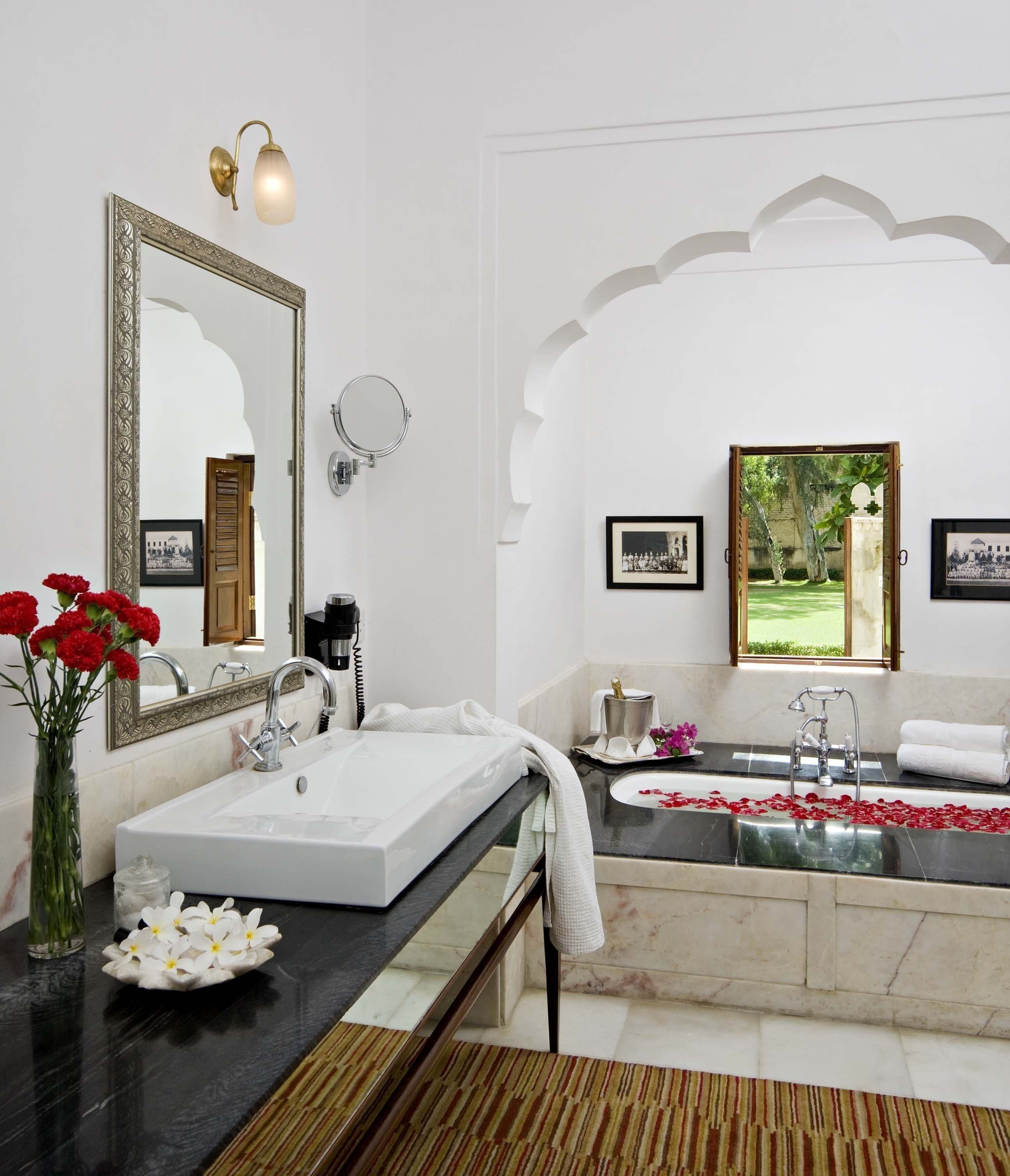 Casa de banho com um espelho grande, duas pias, uma banheira e elementos decorativos como flores e quadros.
