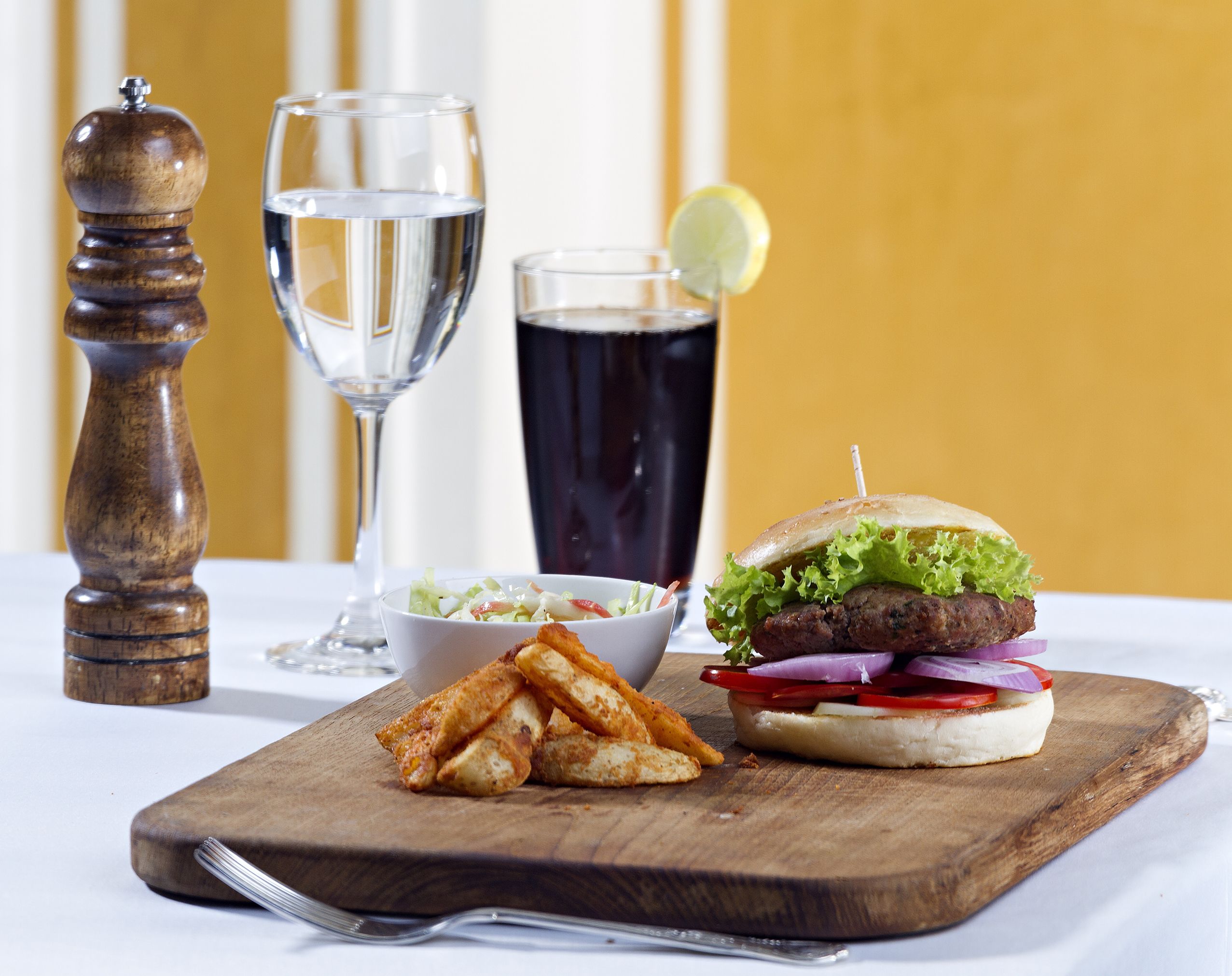 Comida con hamburguesa, papas fritas y una bebida sobre una tabla de madera.